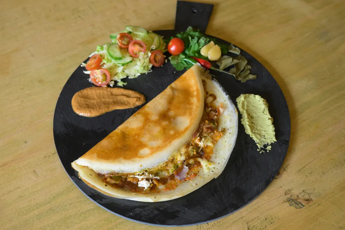 Golden Indian pancake on a serving board with salad and two chutneys