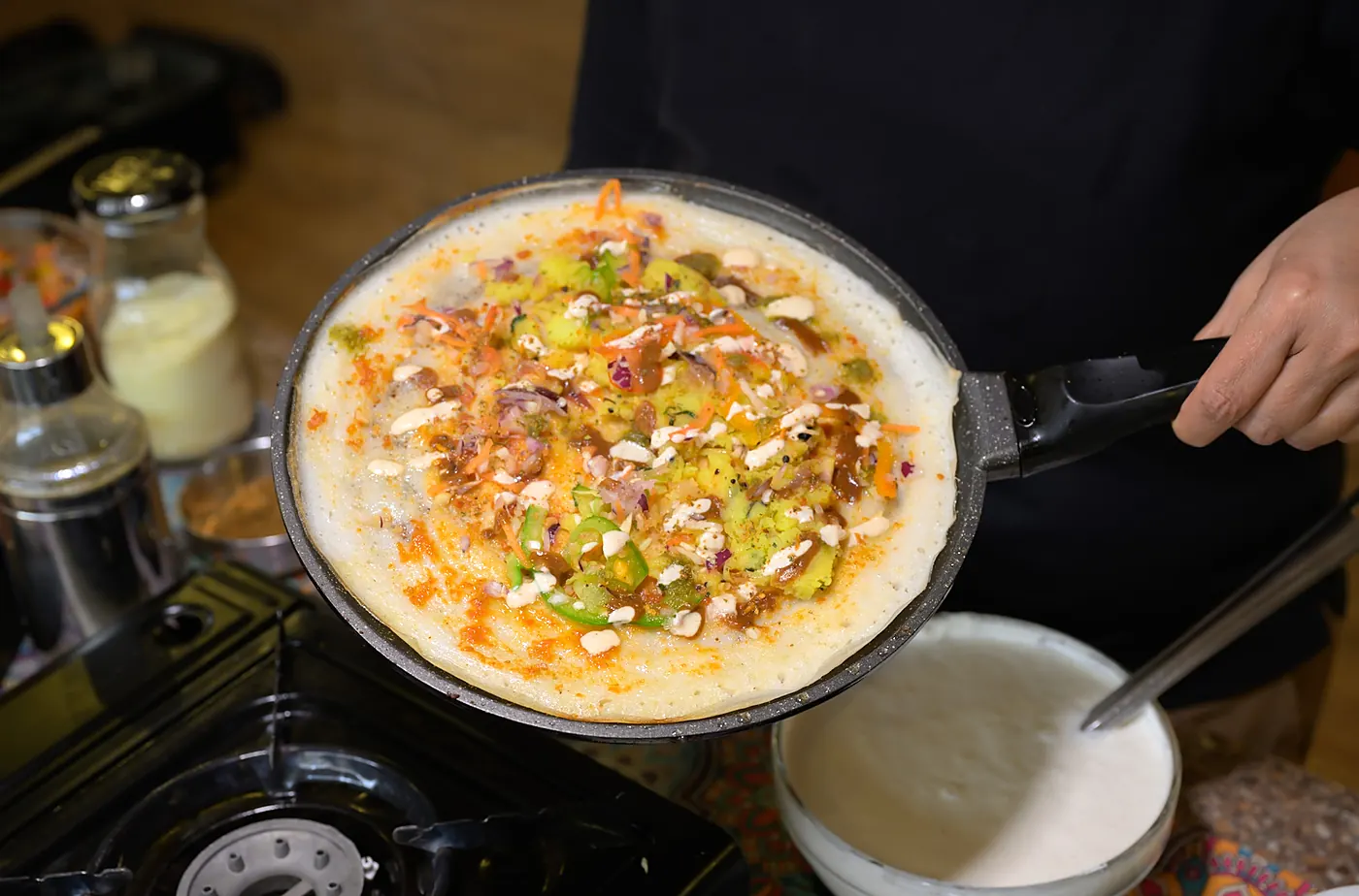 A pancake being cooked to order on the pan, topped with fresh vegetables