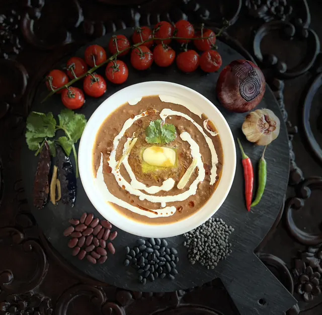 Bowl of home-made dal curry with cream, surrounded by tomatoes and spices