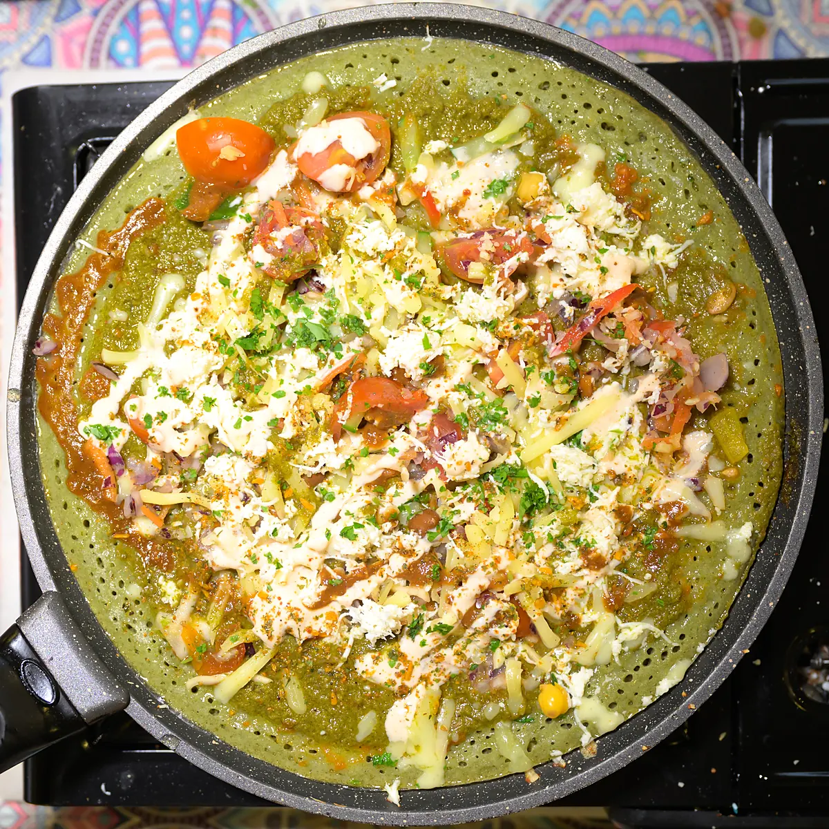 Green herb Indian pancake cooking open on the pan, topped with cheese and vegetables