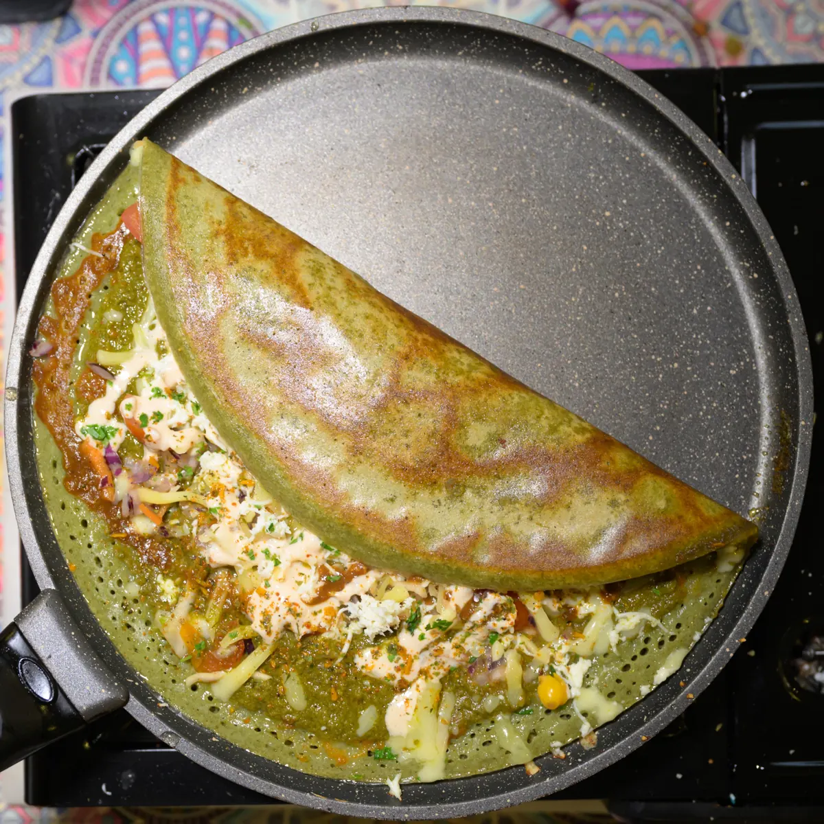Green herb Indian pancake folded on the pan with cheese and fresh herbs