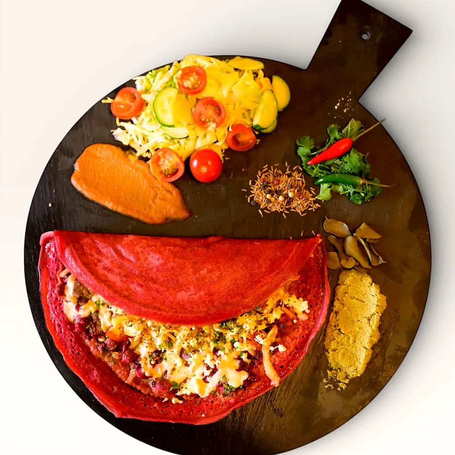 Pink beetroot pancake with hummus and salad on a serving board