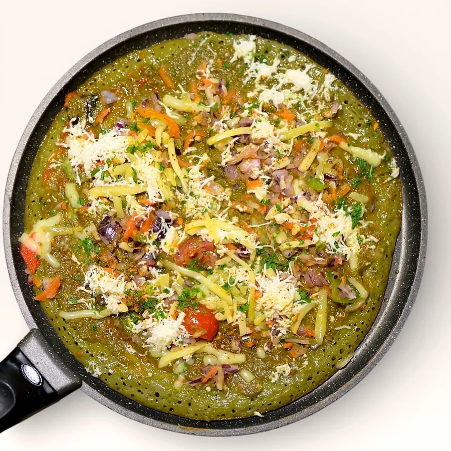 Green herb pancake topped with vegetables and cheese in the pan