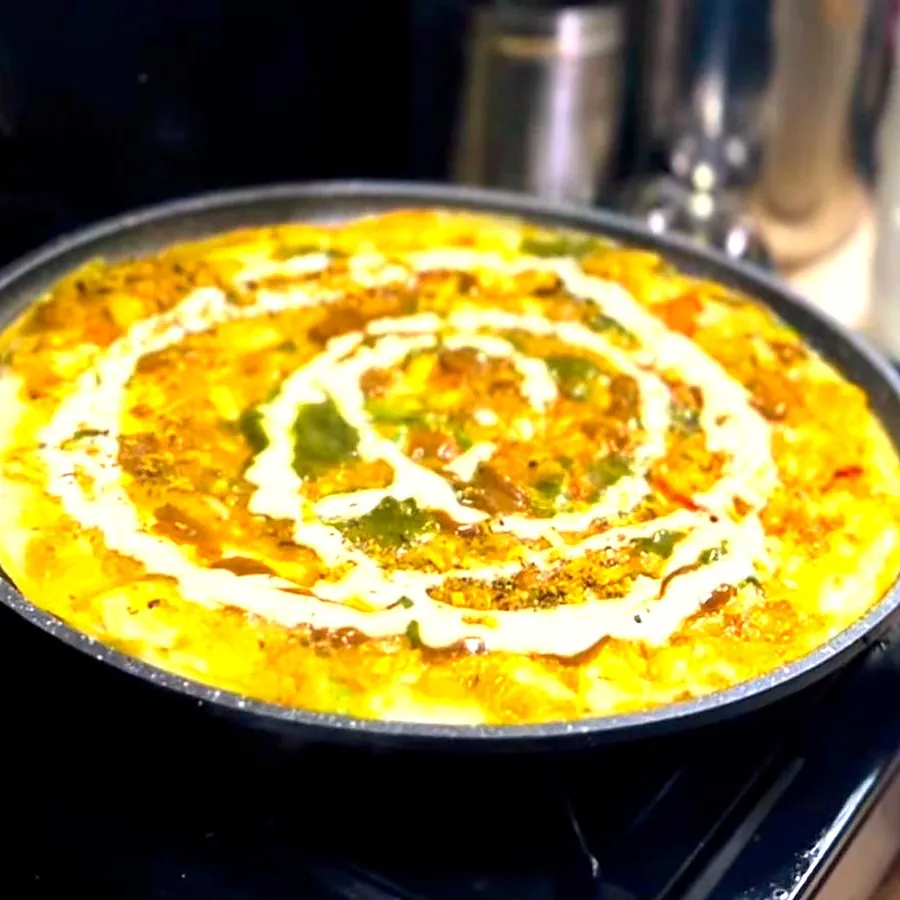 Masala omelette cooking in the pan with a swirl of sauce