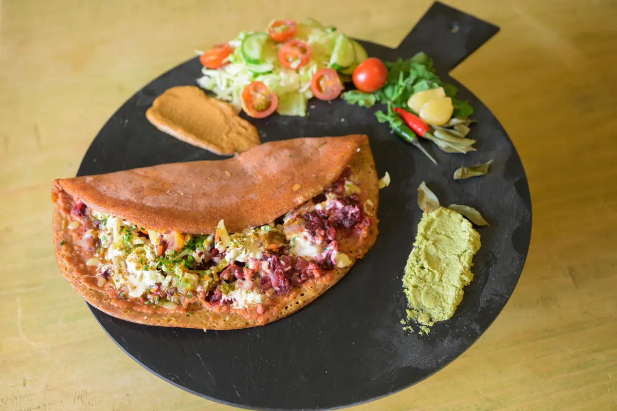 Beetroot Indian pancake on a serving board with salad and chutneys