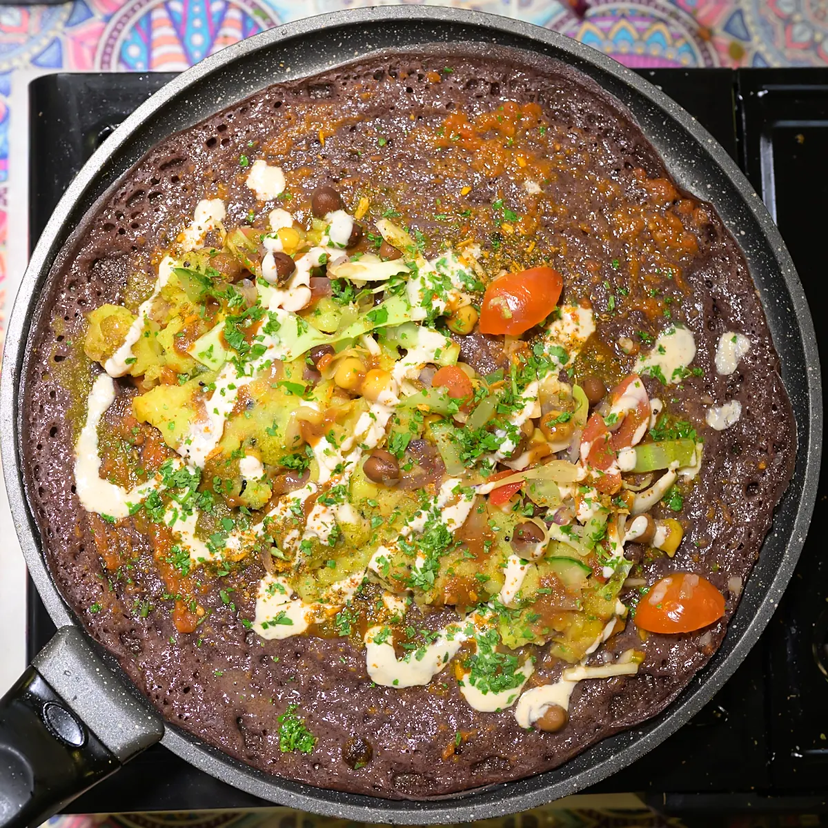 Dark millet Indian pancake on the pan with colourful vegetable toppings