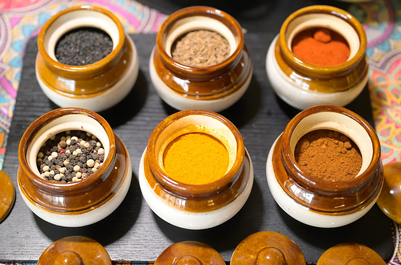 Whole spices in small clay jars: turmeric, chilli, mustard seed and more