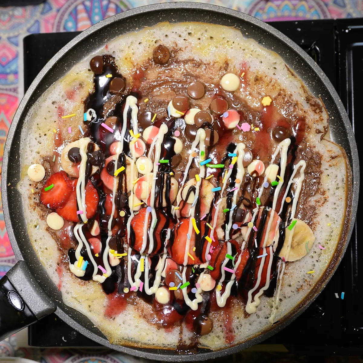 Sweet Indian pancake with strawberries and chocolate drizzle on the pan