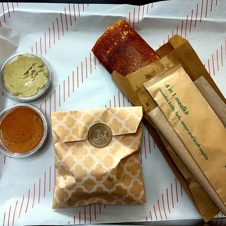Takeaway pancake roll wrapped with two pots of chutney